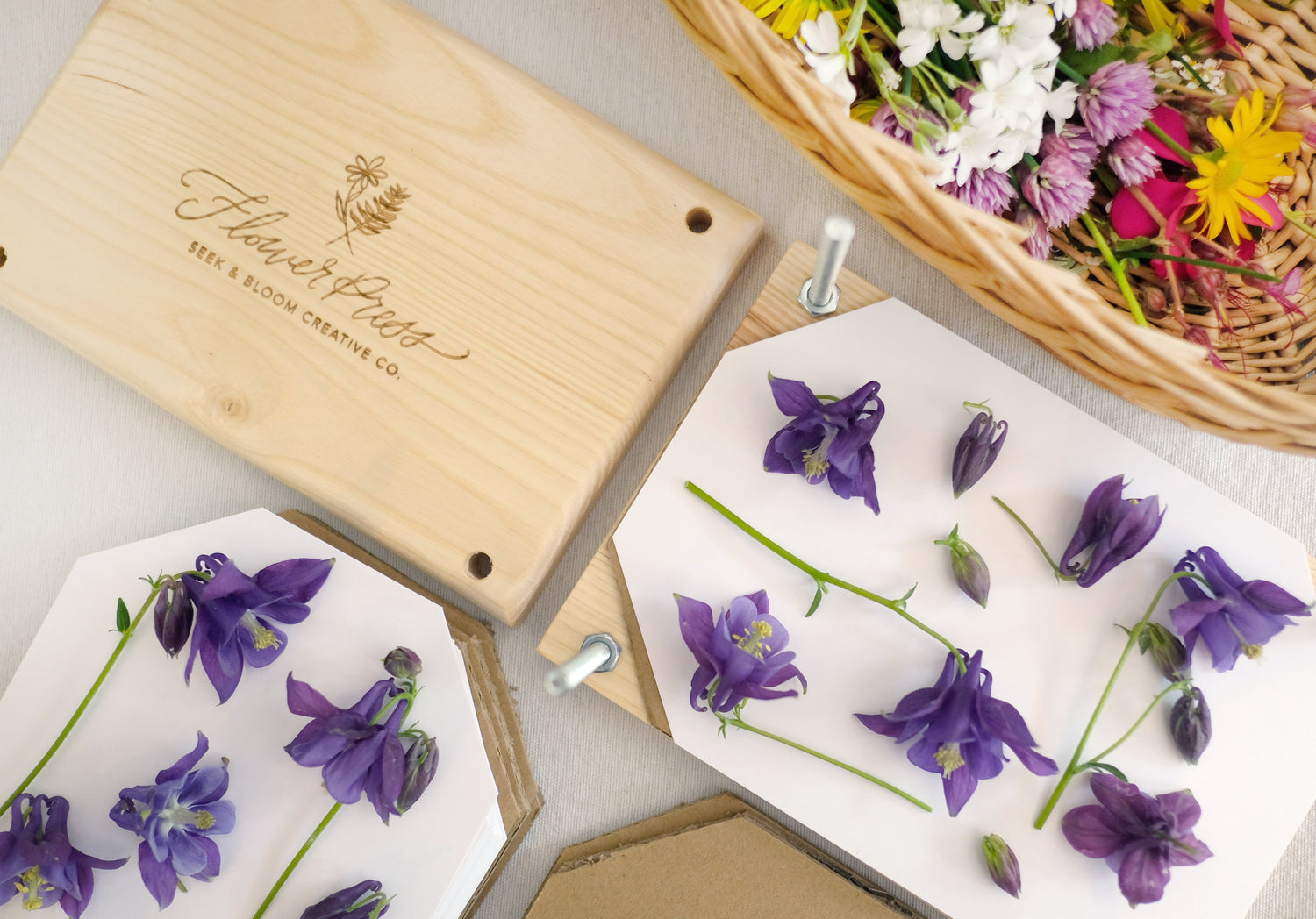 wood flower press engraved with bolts, paper and cardboard and basket of wildflowers from the yard.