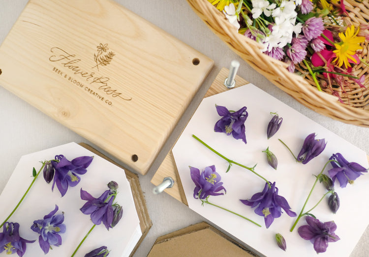 wood flower press engraved with bolts, paper and cardboard and basket of wildflowers from the yard.