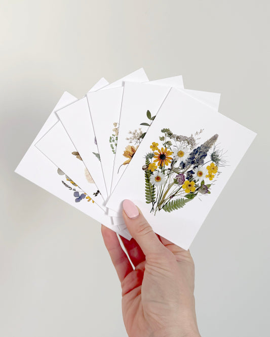 Hand holding a set of floral note cards against a plain background