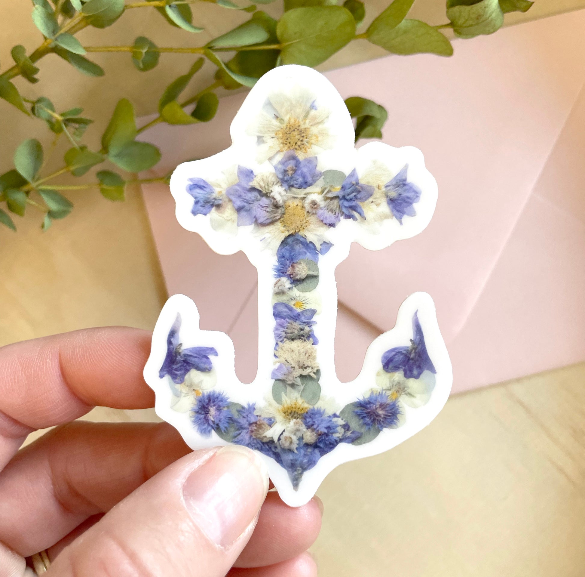 sticker of floral anchor artwork made from blue and white pressed flowers. 
